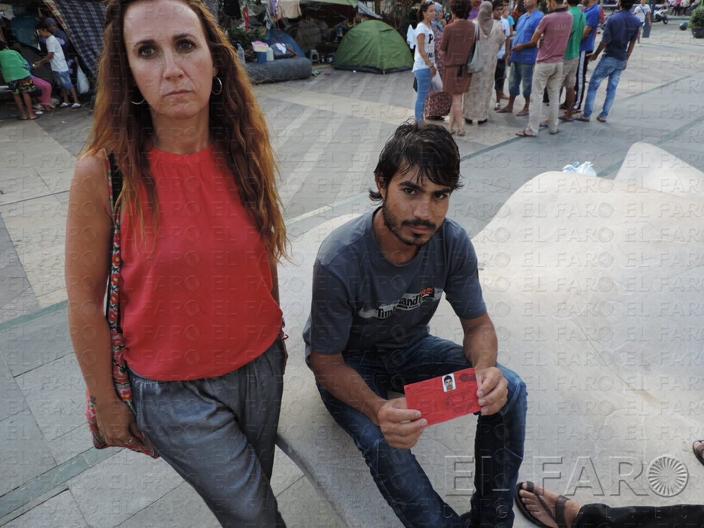 Galán junto a un sirio acampado que muestra su tarjeta de solicitante de asilo.