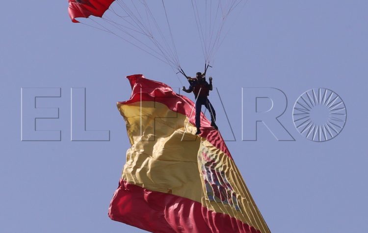 GRA096. MADRID, 12/10/2017.- Un paracaidista con una bandera de España desciende hasta el asfalto del Paseo de la Castellana al inicio del desfile del Día de la Fiesta Nacional que ha sido presidido hoy por los Reyes, y al que ha asistido el Gobierno en pleno, encabezado por Mariano Rajoy, y la mayoría de líderes políticos. El acto consiste en un homenaje a los caídos y un desfile terrestre y aéreo por el paseo de la Castellana, en el que participan unos 3.900 efectivos, entre militares de los tres Ejércitos, guardias civiles, policías y Guardia Real, 84 vehículos y 78 aeronaves. EFE/Kiko Huesca