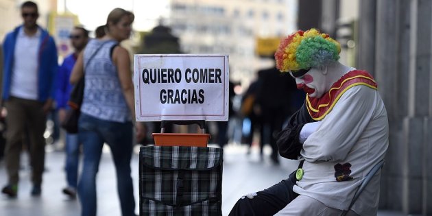 Rayito, a beggar dressed as a clown sits next to a placard reading "I want to eat, thank you" in Gran Via street, in the centre of Madrid, on October 28, 2014. AFP PHOTO/ GERARD JULIEN (Photo credit should read GERARD JULIEN/AFP/Getty Images)
