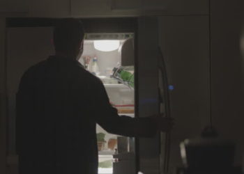 Young man opening the refrigerator at night, removing food, and closing it