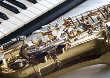 Rusty old classical saxophone on marble table next to electric piano keyboard