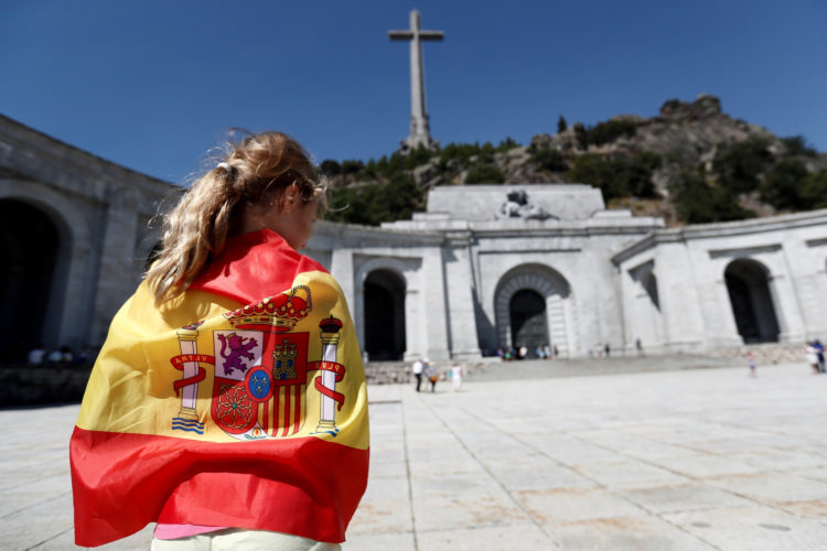 GRAF8433 MADRID (Comunidad de Madrid), 21/8/2018.-Una persona envuelta en una bandera en la explanada del Valle de los Caídos. El Gobierno aprobará el próximo viernes un decreto que modificará la Ley de Memoria Histórica para permitir la exhumación de los restos mortales de Francisco Franco del Valle de los Caídos, un polémico monumento que el dictador ordenó erigir.El ministro de Cultura y Deporte, José Guirao, confirmó hoy esa medida, aunque al tratarse de un decreto ley tendrá que ser validado por el Parlamento, lo que no ocurrirá al menos hasta septiembre.EFE/Mariscal